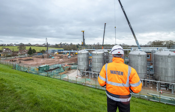 Water engineer stood with hard hat and high vis looking out onto a water recycling centre