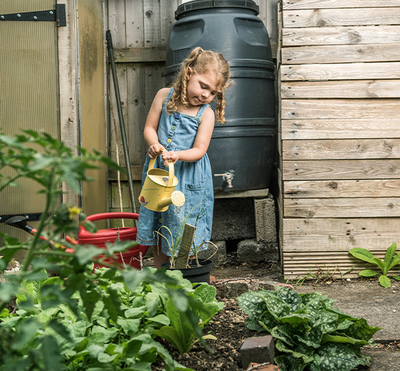 Girl in the garden watering plants with a small yellow watering can
