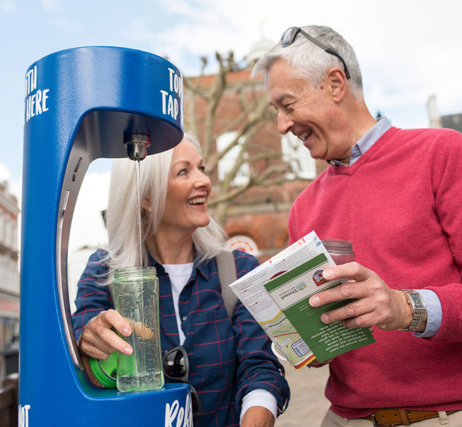 Couple stood next to a Wessex Water refill point smiling and filling up their bottle
